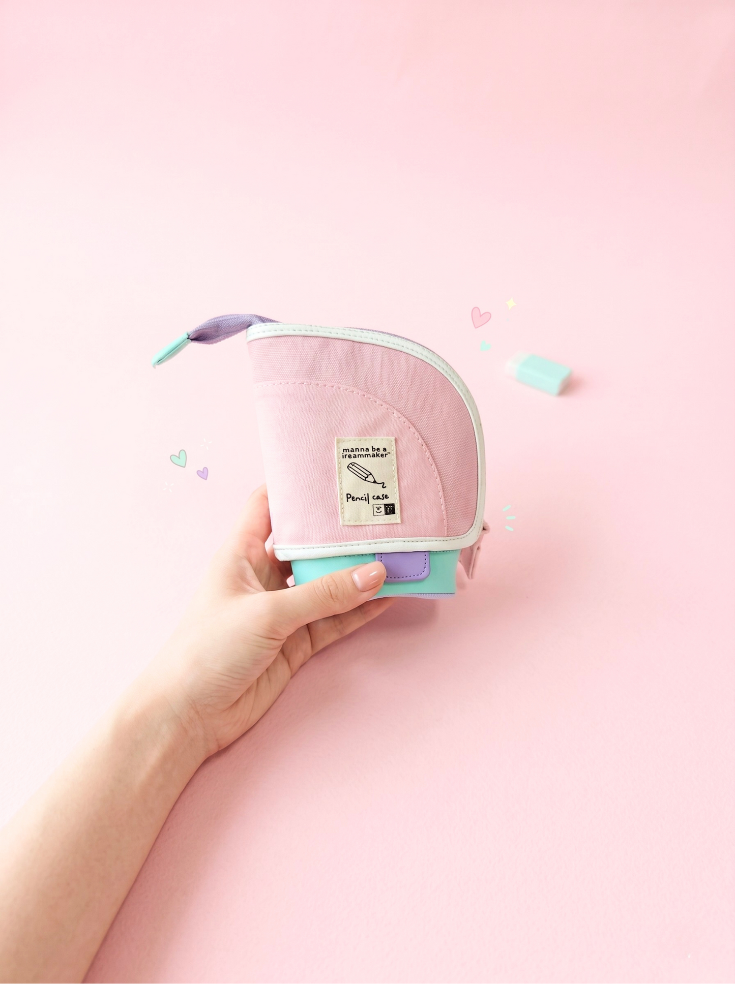 Hand holding a small pink and green container with a lid on a pink background
