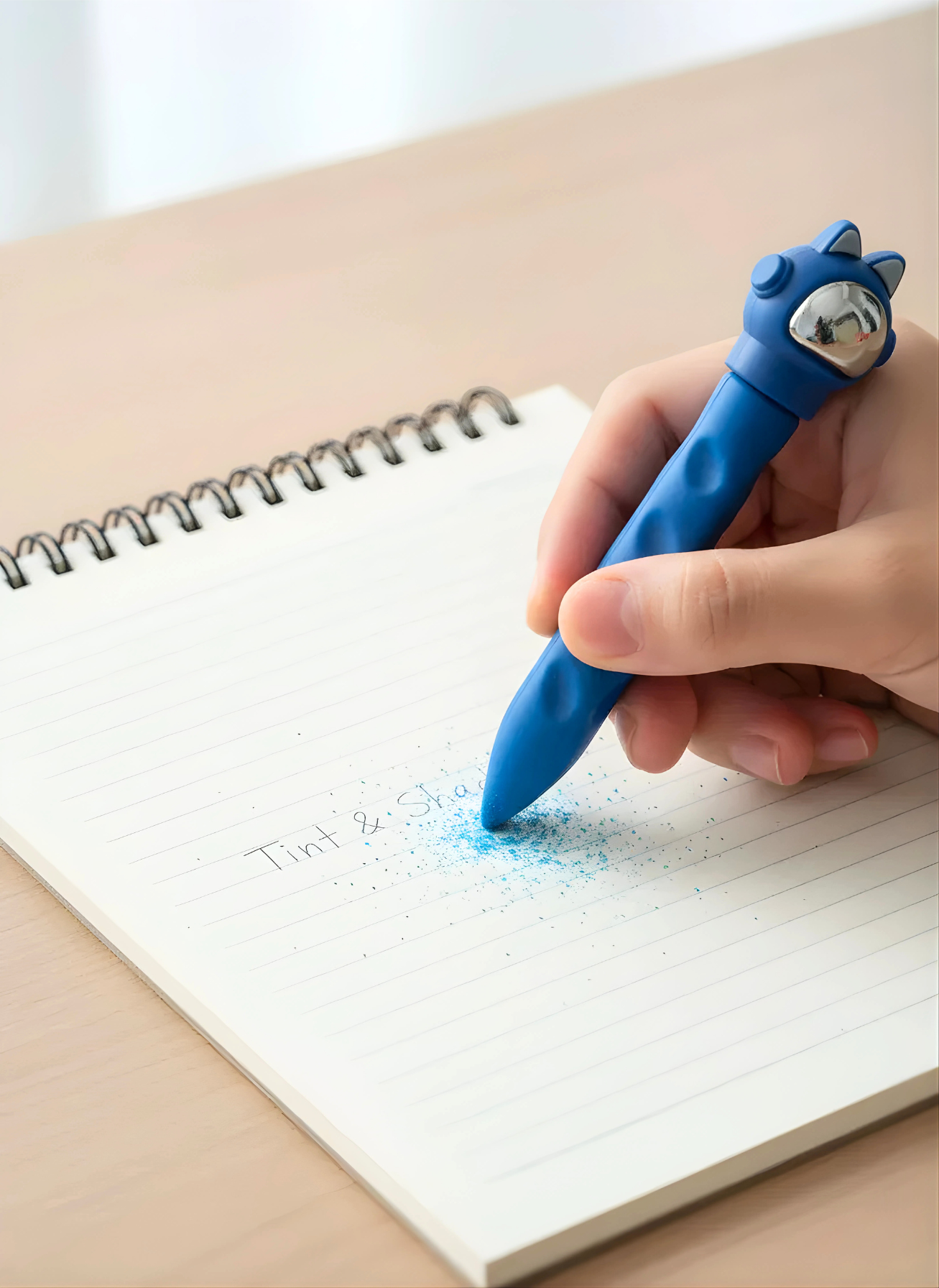 Hand holding a blue pen with a cat design, writing on a notebook.