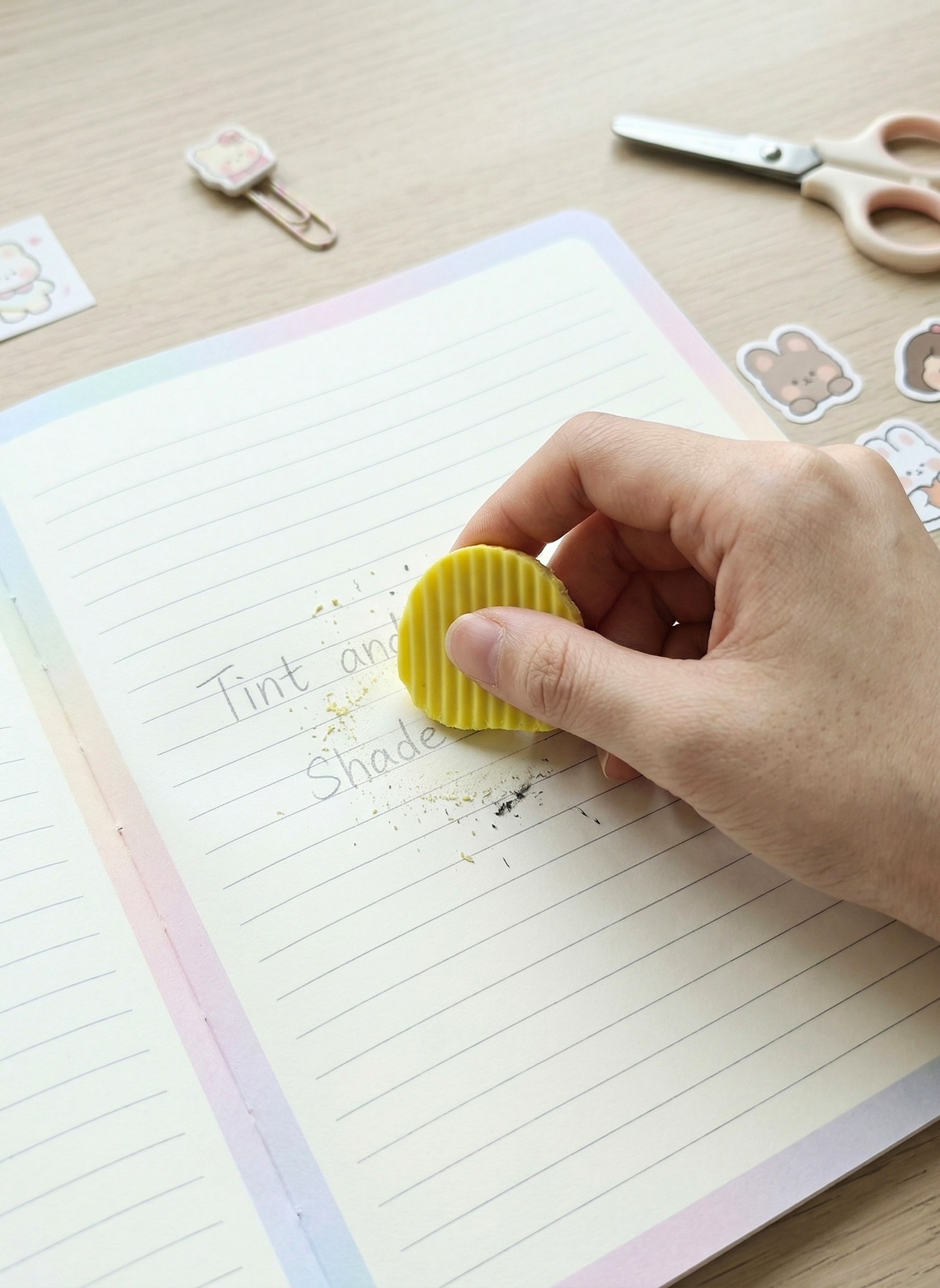 Hand using a yellow eraser on a notebook with stationery items in the background