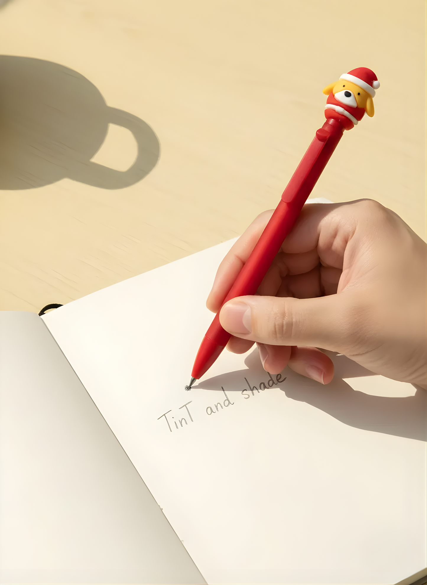 Hand holding a red pen with a cartoon character on top, writing in a notebook.