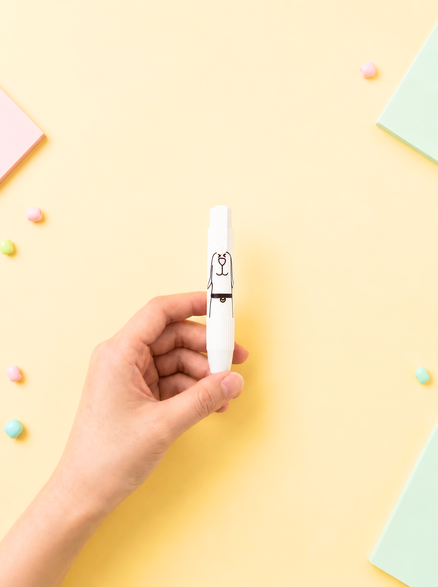 Hand holding a white pen with a cat design on a yellow background