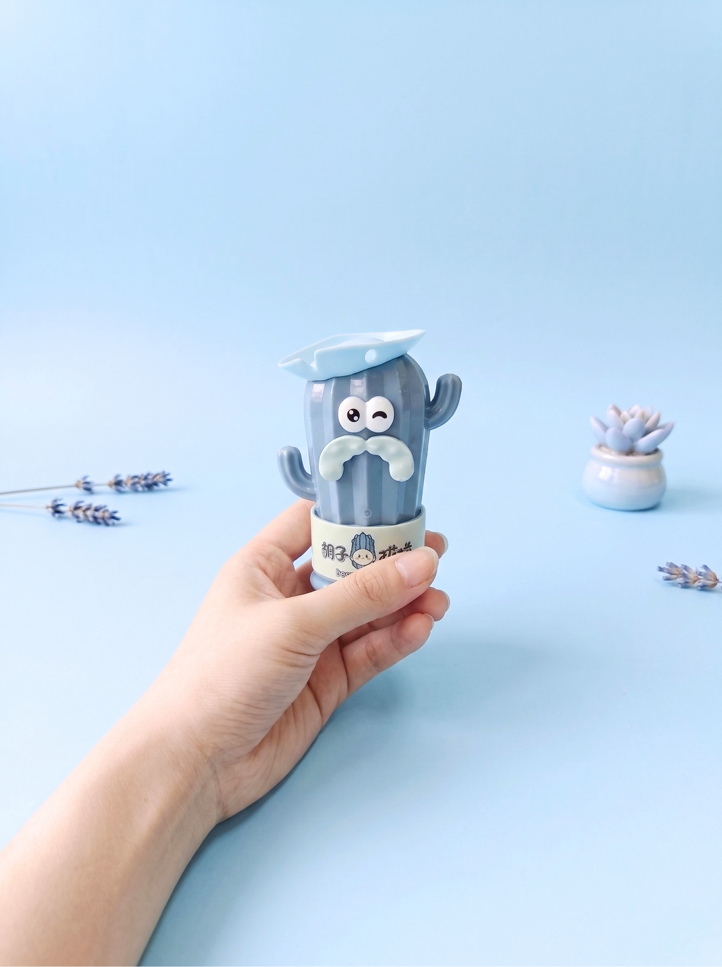 Hand holding a small blue container with a cartoon character on a light blue background