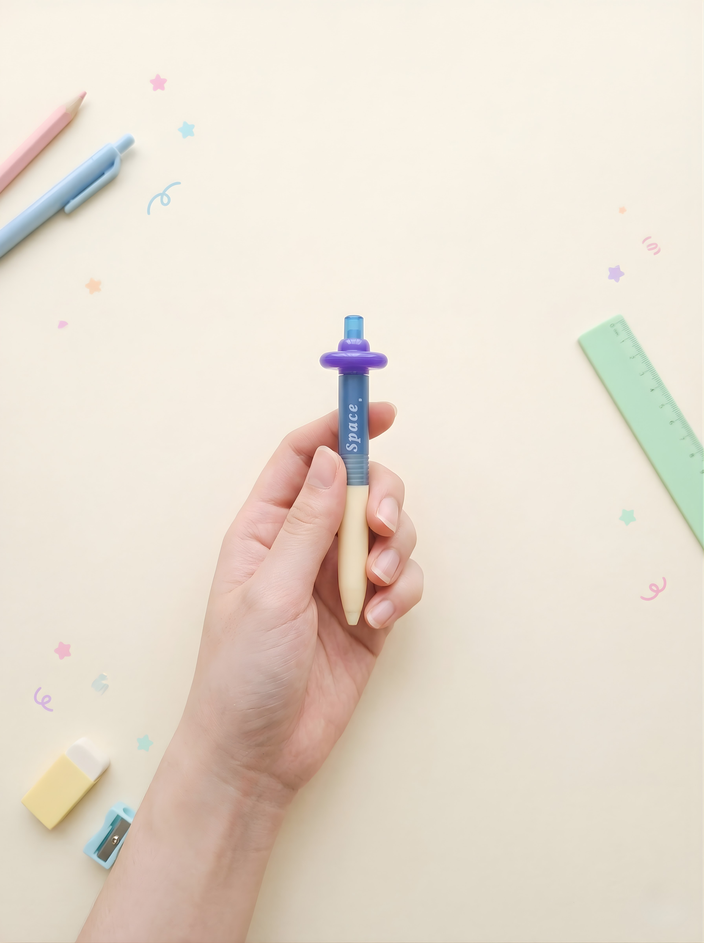 Hand holding a pen with colorful stationery items on a light background