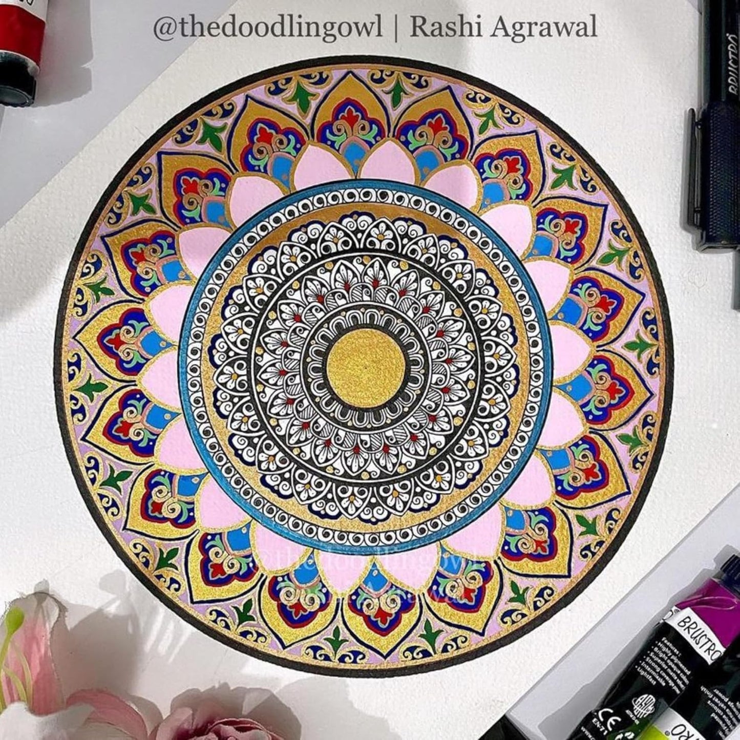 Colorful mandala drawing on a white surface with art supplies around