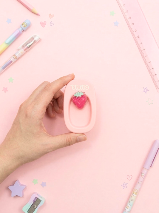 Hand holding a pink strawberry-shaped eraser with stationery items on a pink background