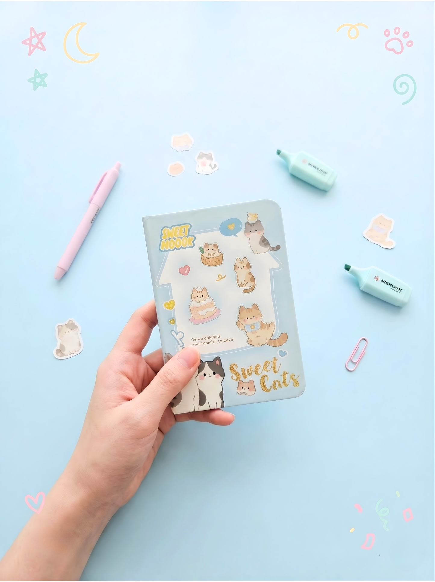 Hand holding a pack of 'Sweet Cats' stickers on a light blue background with stationery items.