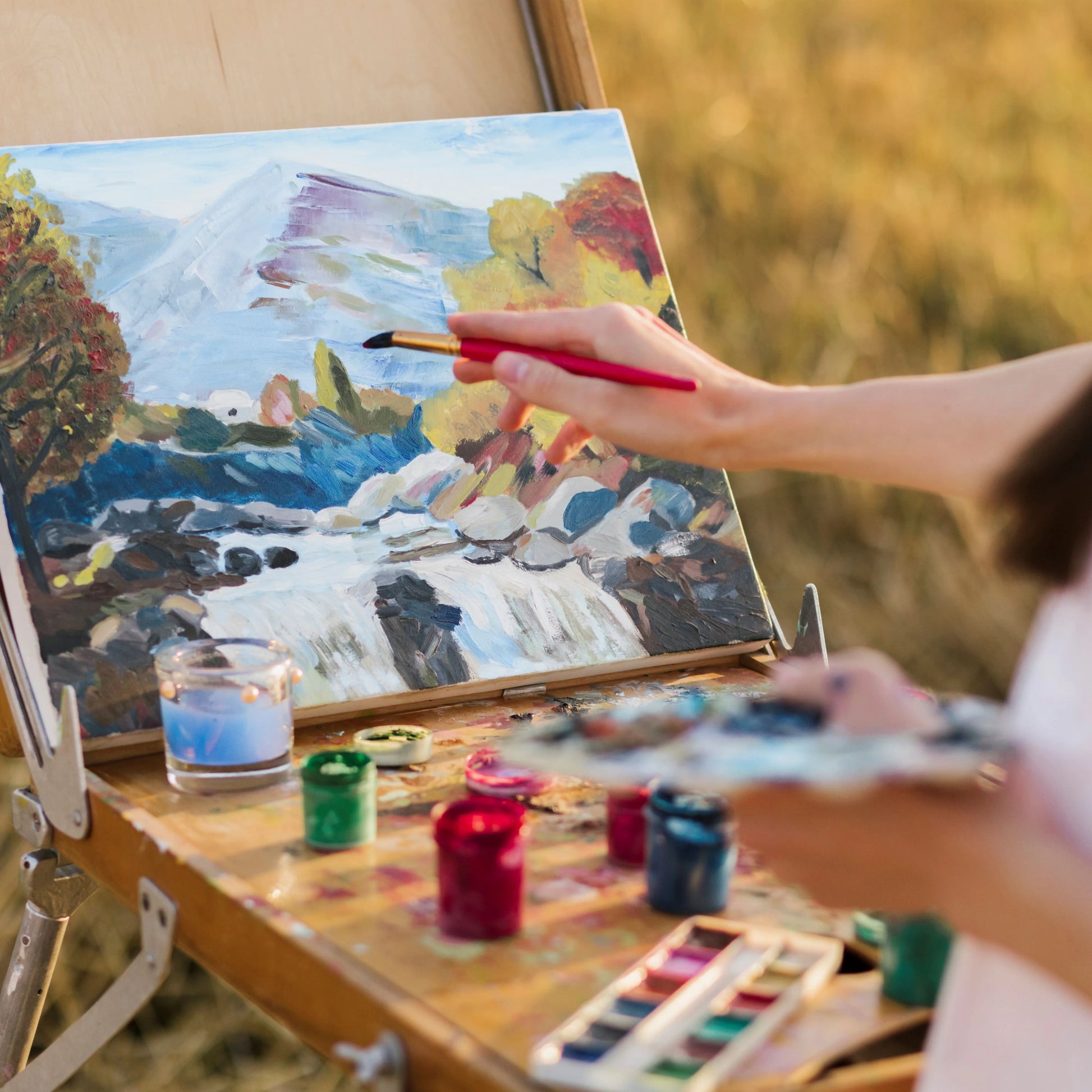 Person painting a landscape scene with trees and mountains using watercolors.