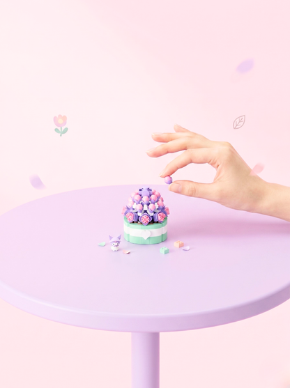 Pastel-colored cupcake on a small round table with a hand reaching towards it against a light pink background.