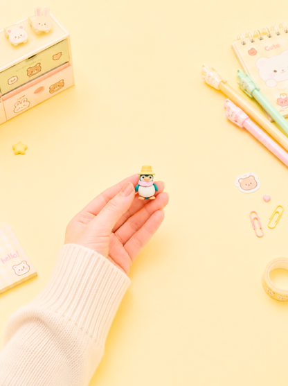 Hand holding a small figurine on a yellow background with stationery items