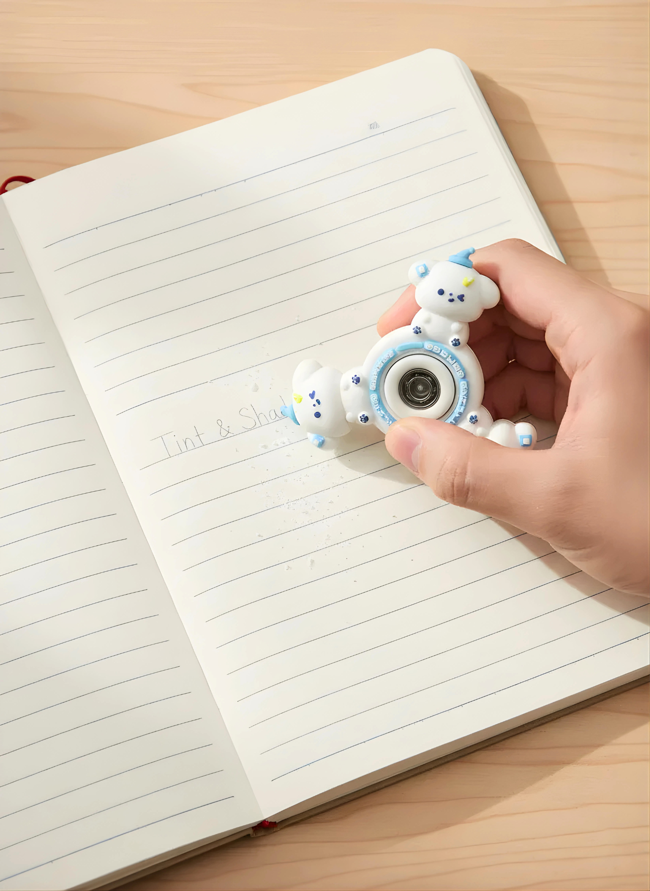 Hand holding a small blue and white fidget spinner over an open notebook on a wooden surface