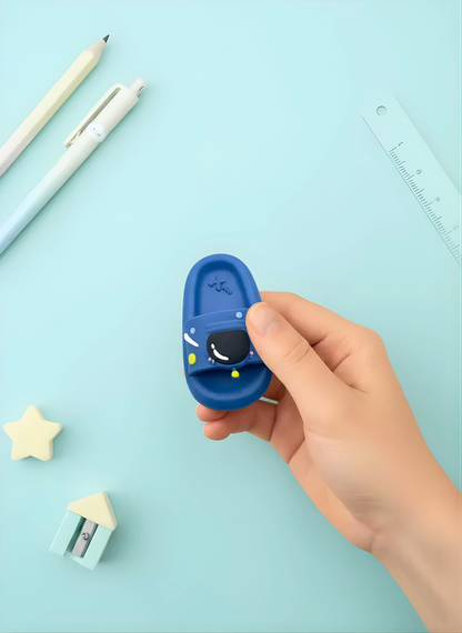 Hand holding a blue cartoon character eraser with stationery items on a light blue background