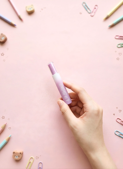 Hand holding a pink and white marker on a pink background with stationery items.