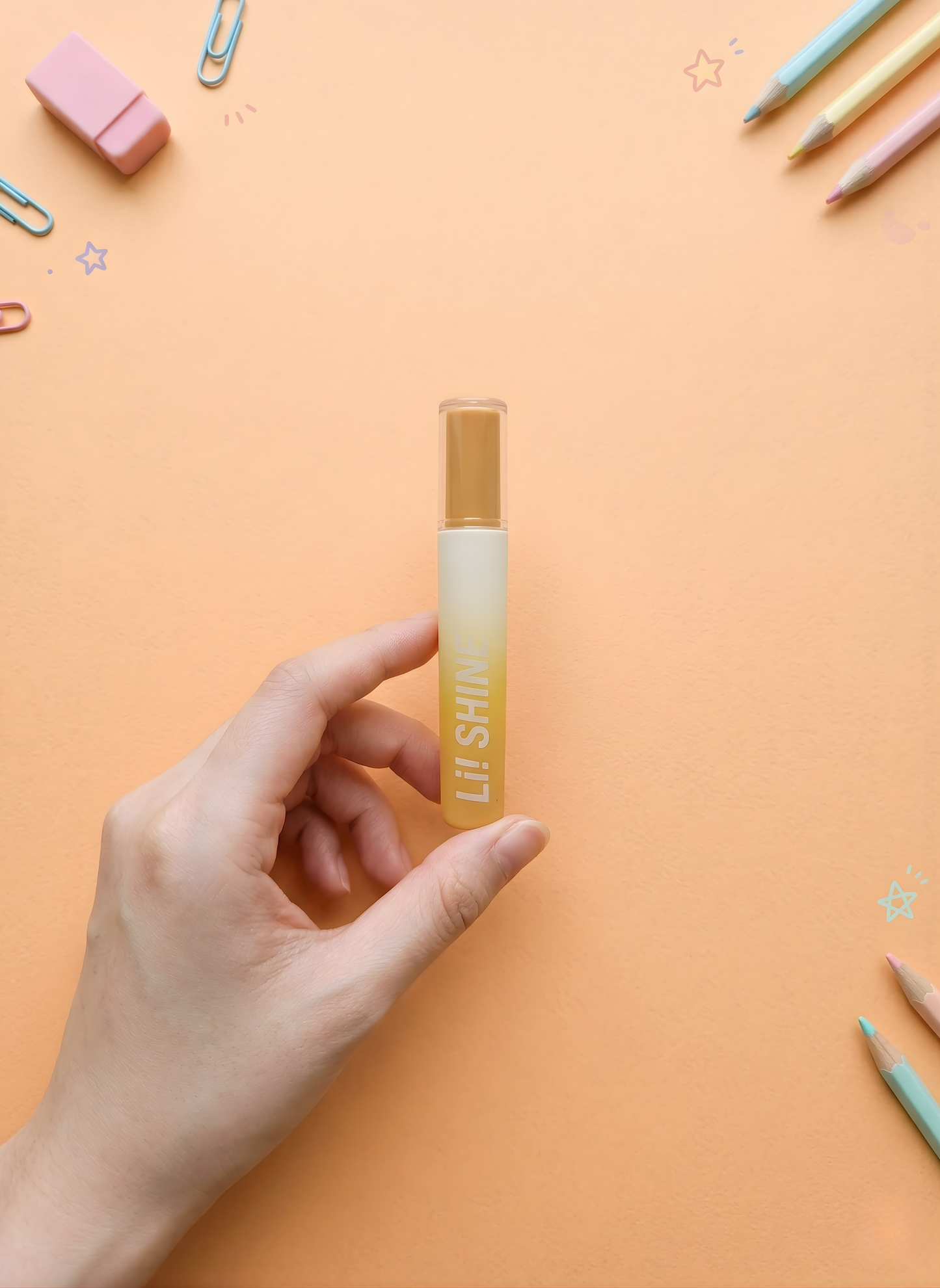 Hand holding a lip balm with 'Lil Shiny' branding on an orange background
