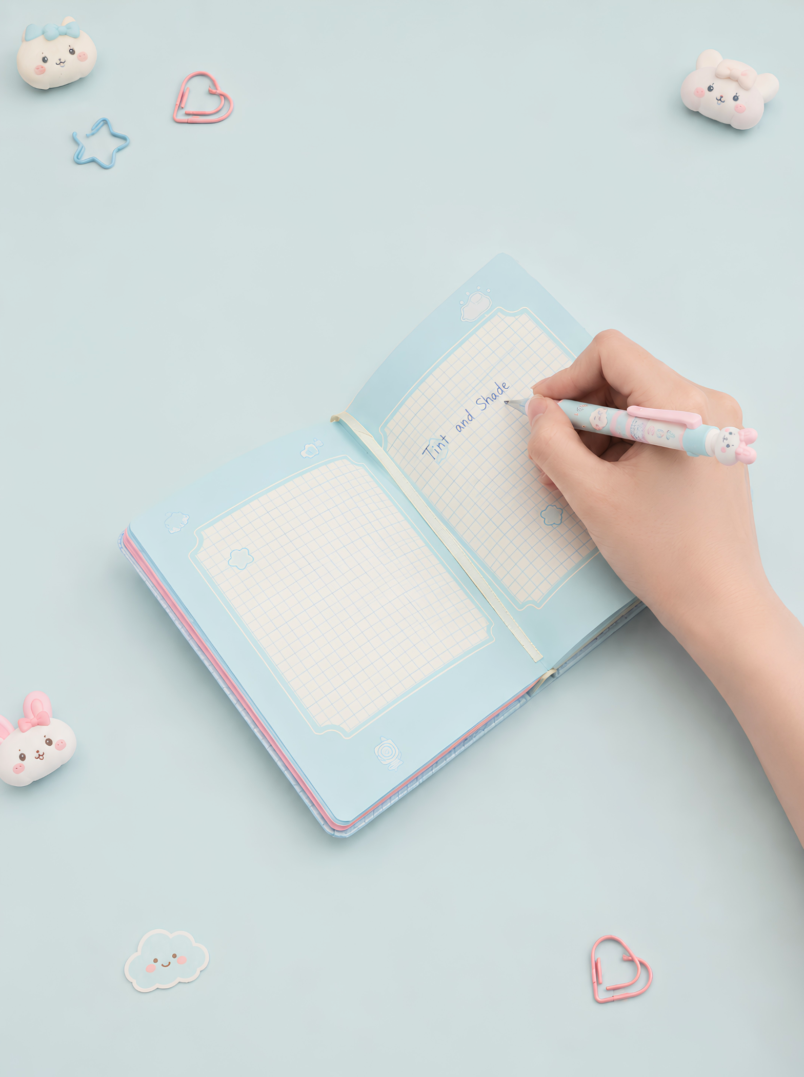 Hand writing in a light blue notebook with decorative paper clips on a light blue background