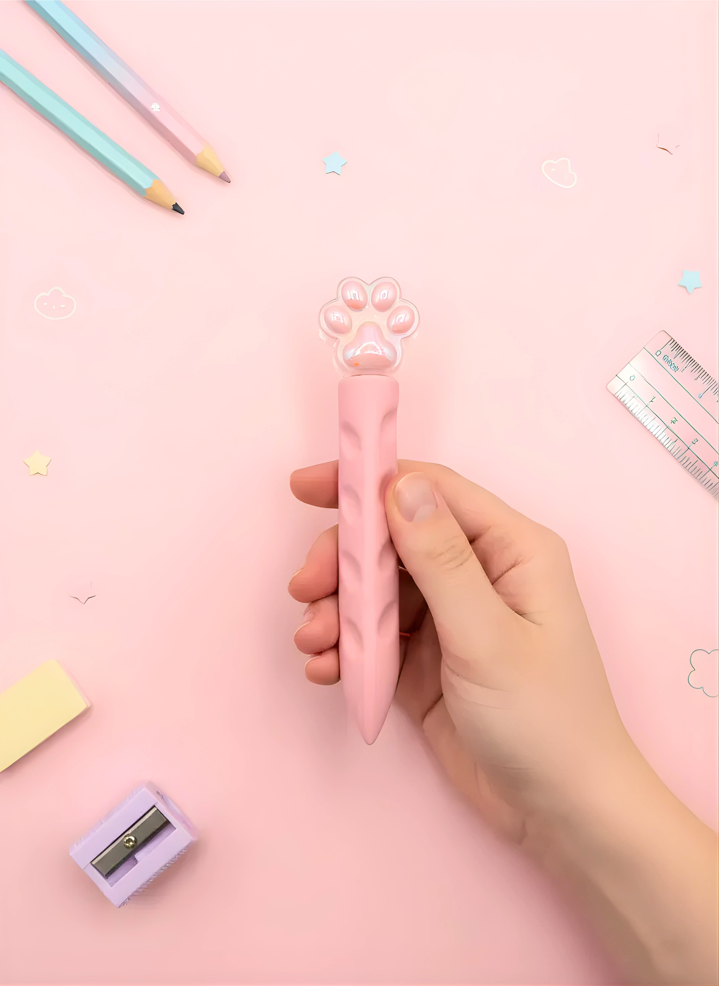 Hand holding a pink pencil sharpener with stationery items on a pink background