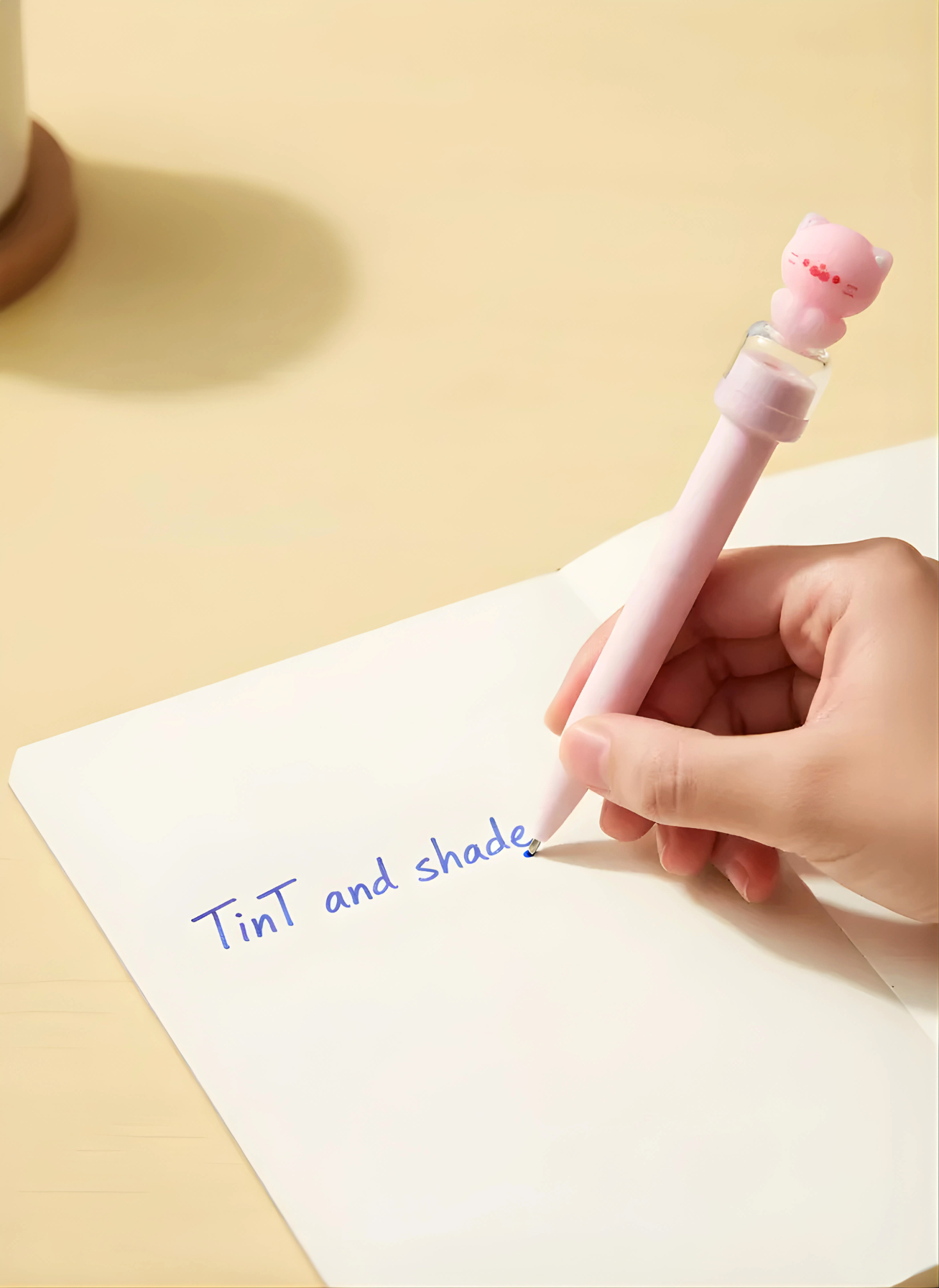 Person writing on a notepad with a pink pen featuring a cat-shaped clip.