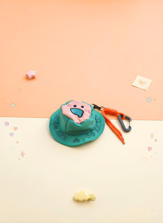 Small plush toy with a pink face and green hat on a peach and white gradient background