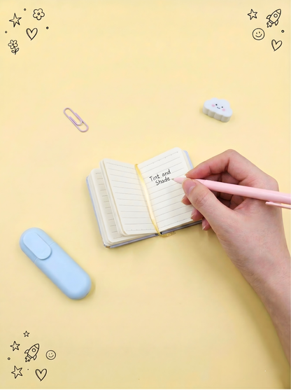 Hand holding a pink pen over a small notebook on a yellow background with decorative elements.