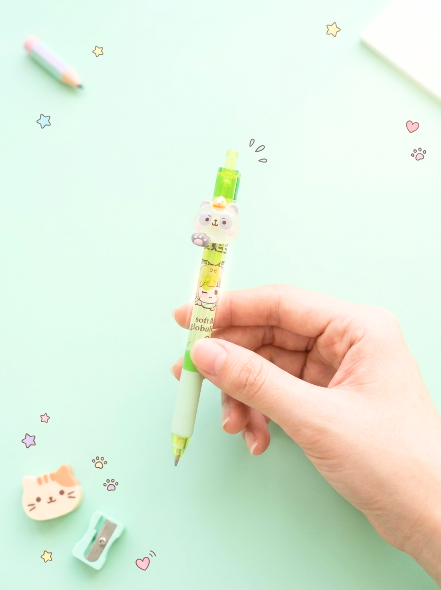 Hand holding a green mechanical pencil with a cat design on a light green background