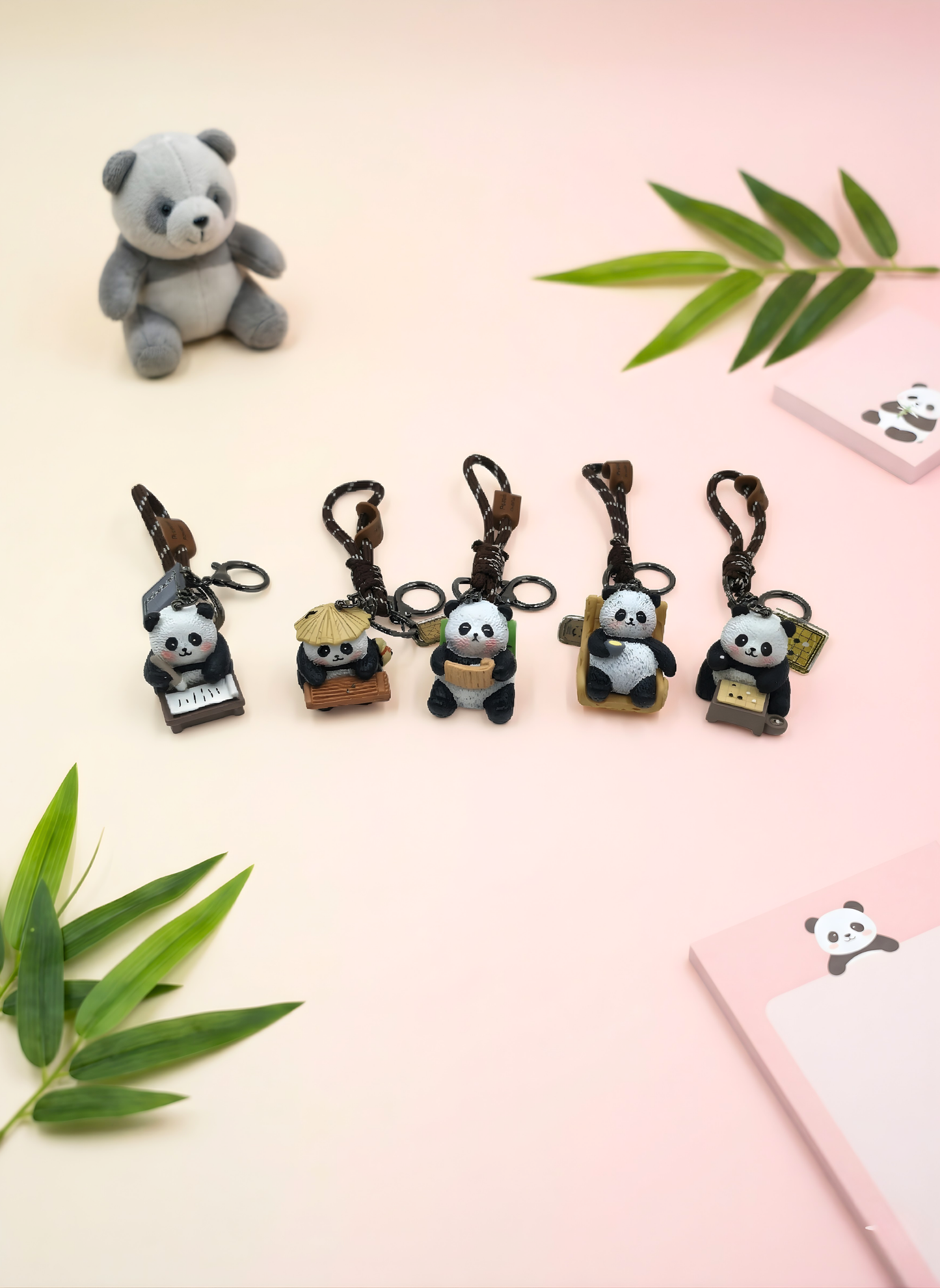 Set of panda keychains on a light pink background with green leaves.
