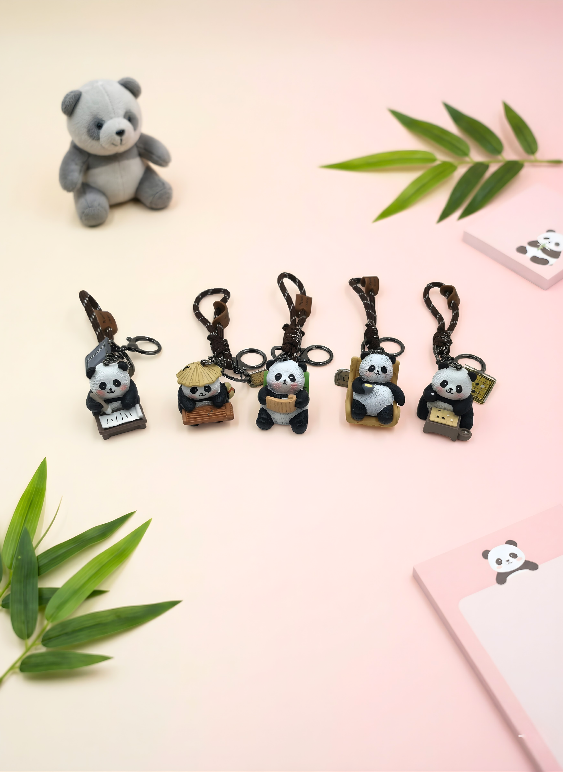 Set of panda keychains on a light pink background with green leaves.