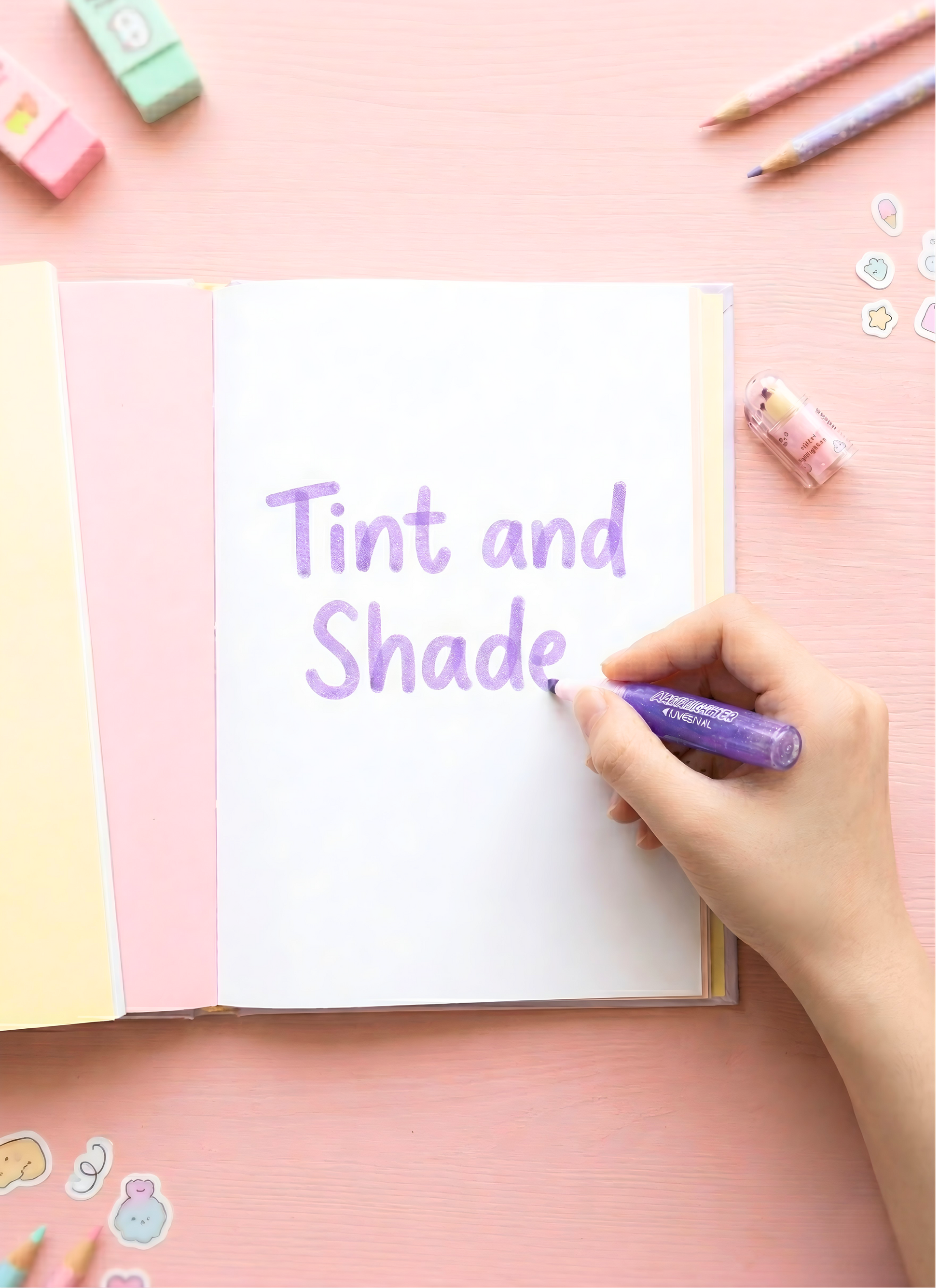 Hand writing 'Tint and Shade' with a purple marker on a pink surface with stationery items.