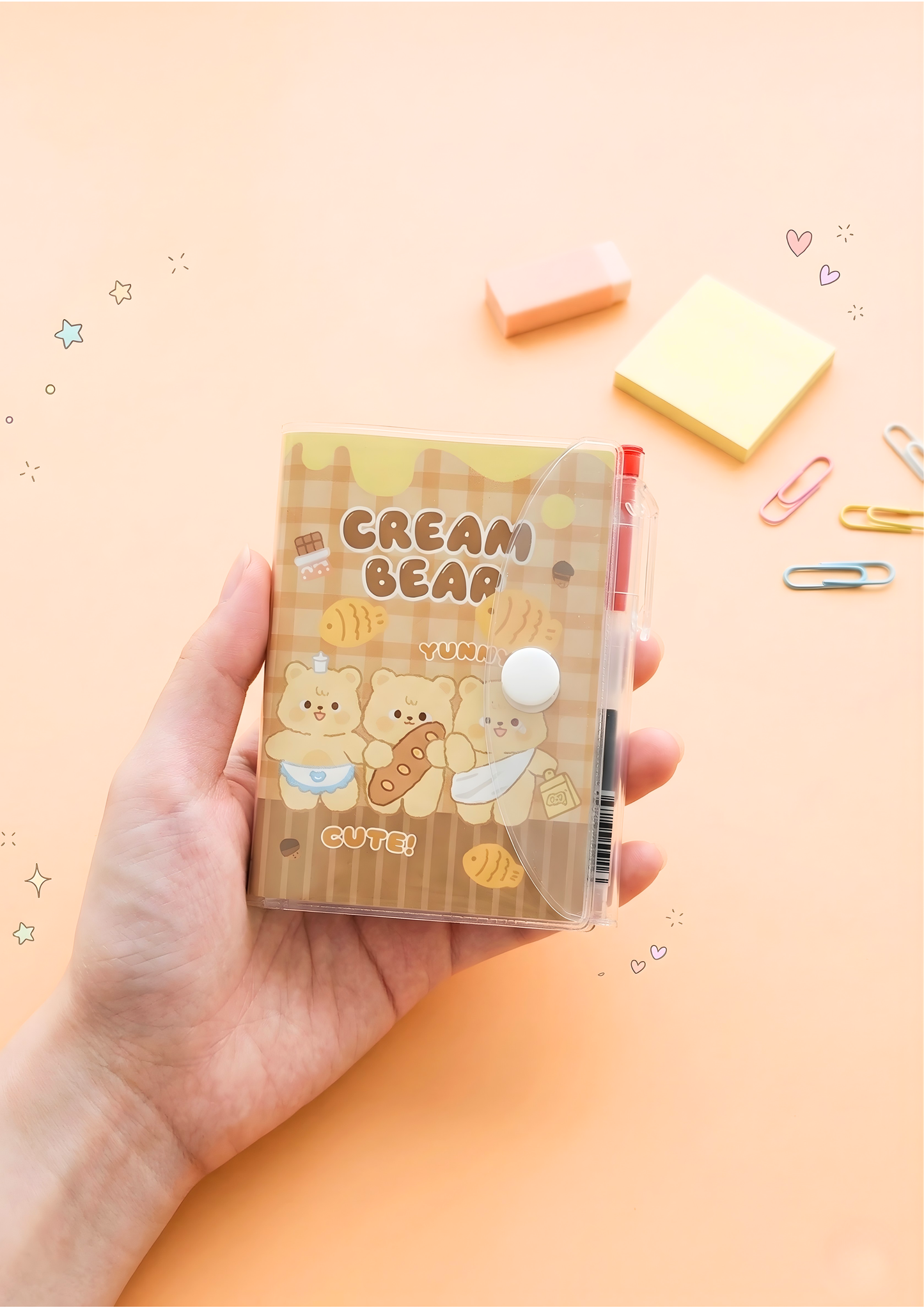 Hand holding a small notebook with 'Cream Bear' design on a light orange background