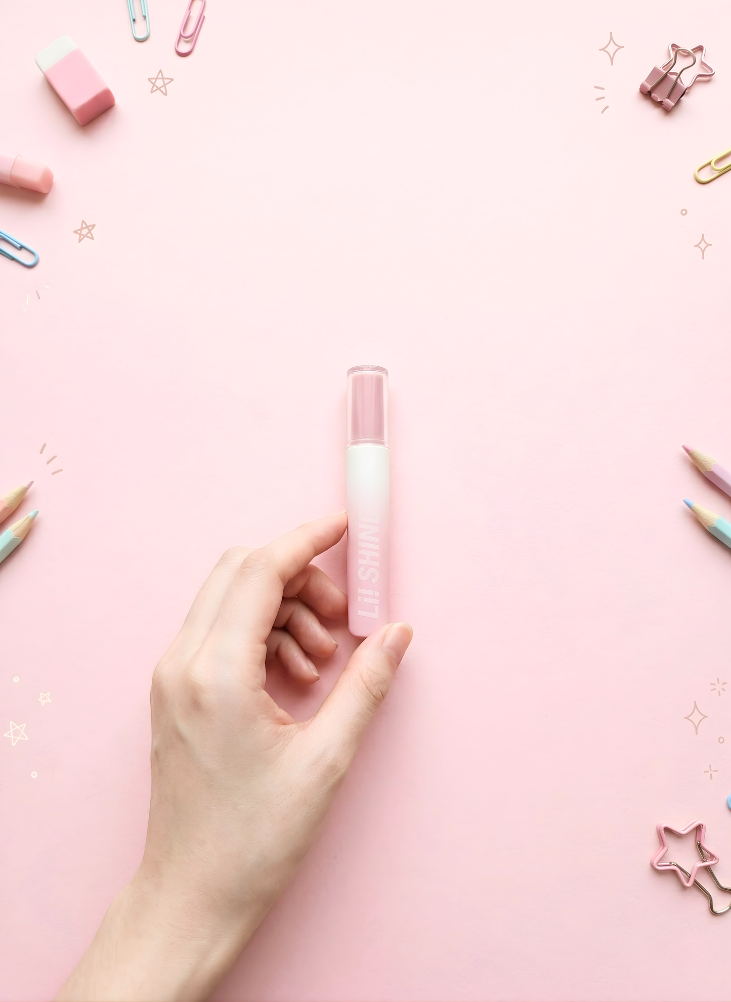 Hand holding a pink lip balm against a pink background with stationery items.