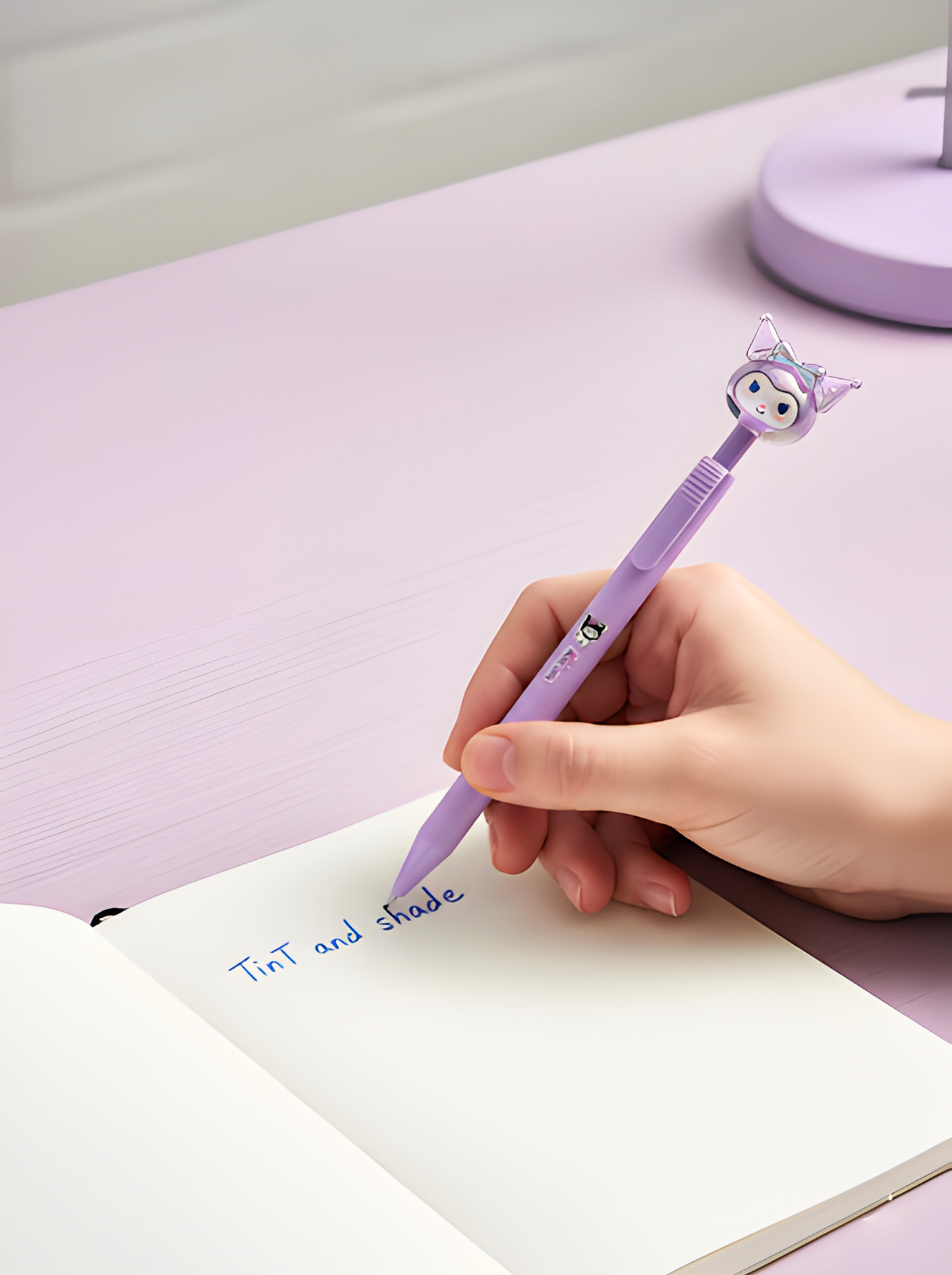 Hand holding a purple pen with a cat design, writing in a notebook on a pink surface.