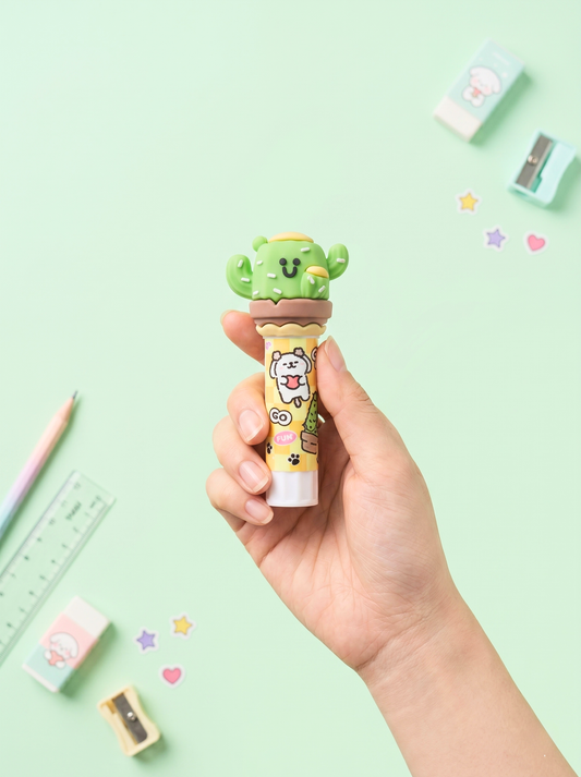 Hand holding a cute green cactus-shaped lip balm with cartoon character on a light green background.