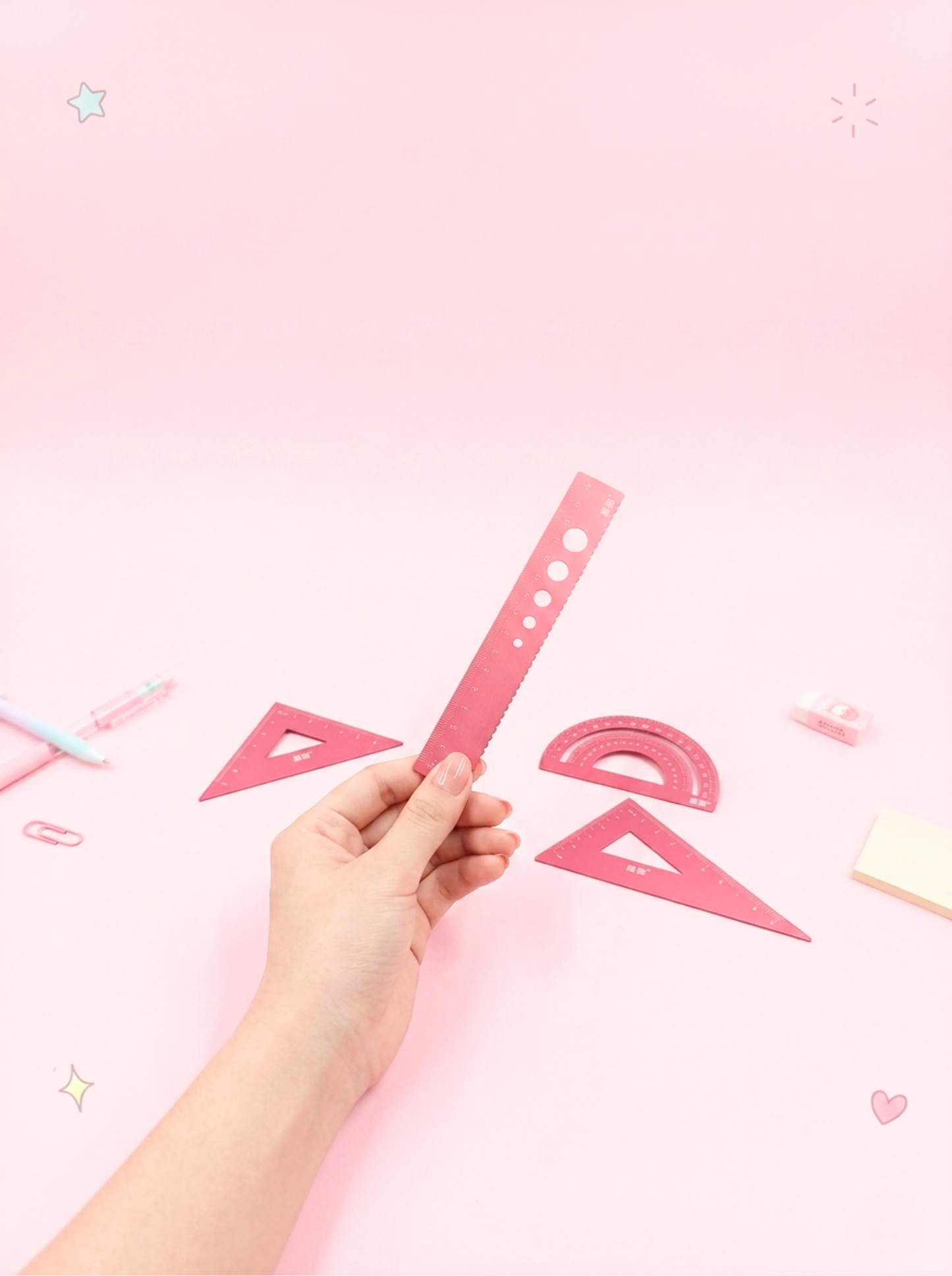 Hand holding a pink ruler against a pink background with geometric shapes.