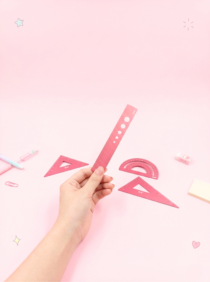 Hand holding a pink ruler against a pink background with geometric shapes.