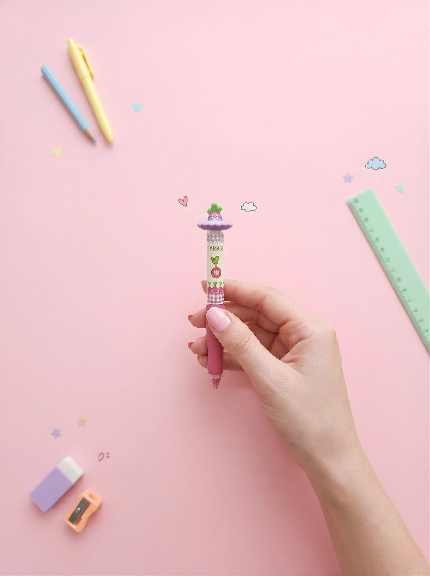 Hand holding a colorful pen with stationery items on a pink background