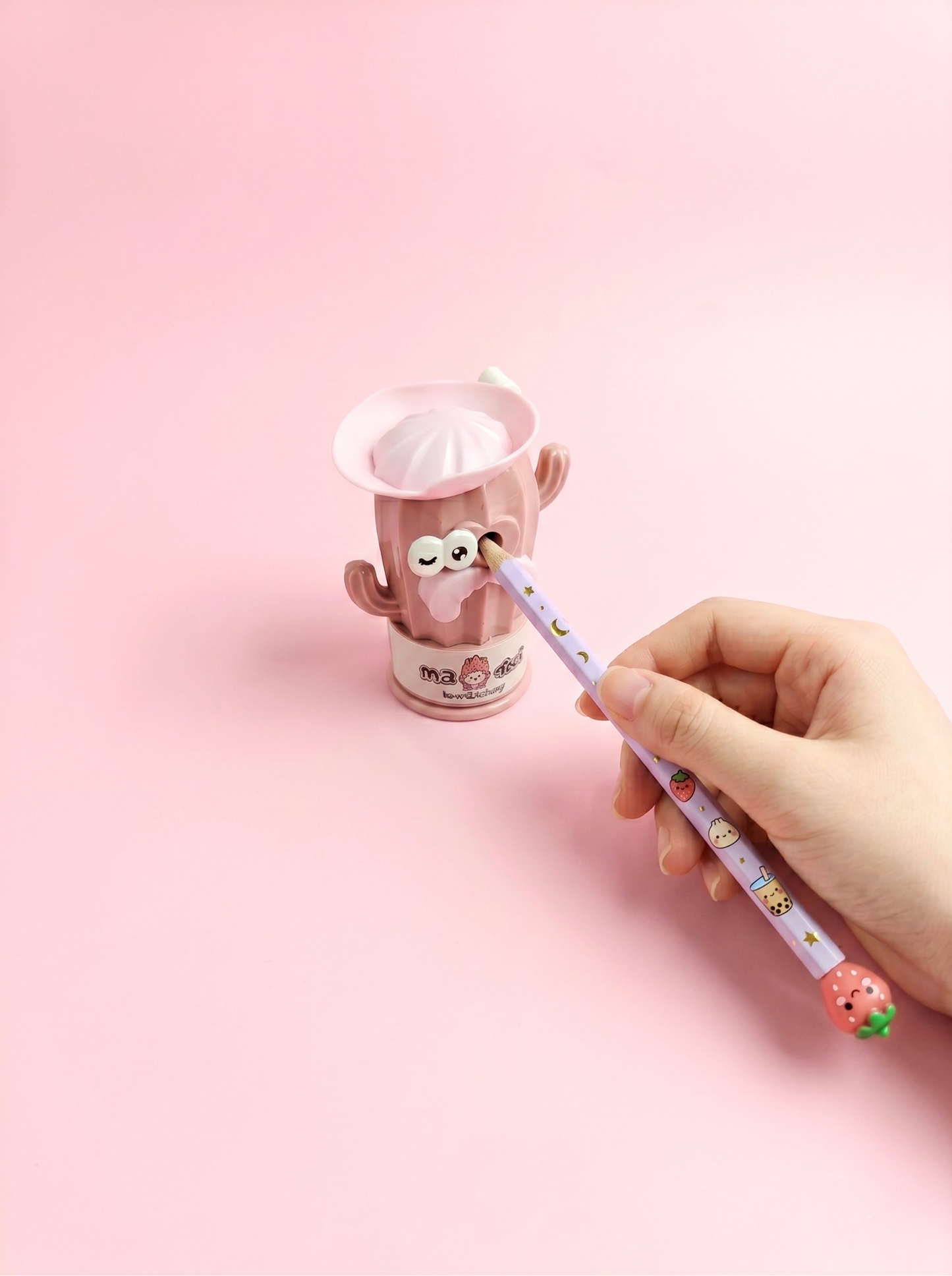 Hand holding a cute pen with a small cup in the background on a pink background