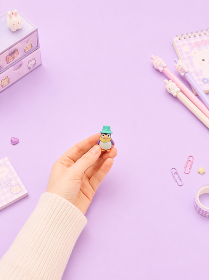 Hand holding a small figurine of a penguin on a purple background with stationery items.