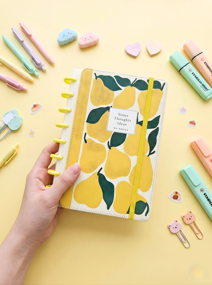 Notebook with pear design held by a hand on a yellow background with stationery items.
