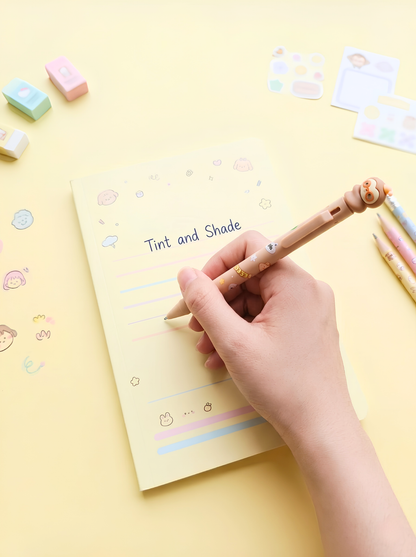 Hand holding a pen over a notepad with 'Tint and Shade' text on a yellow background with stationery items.