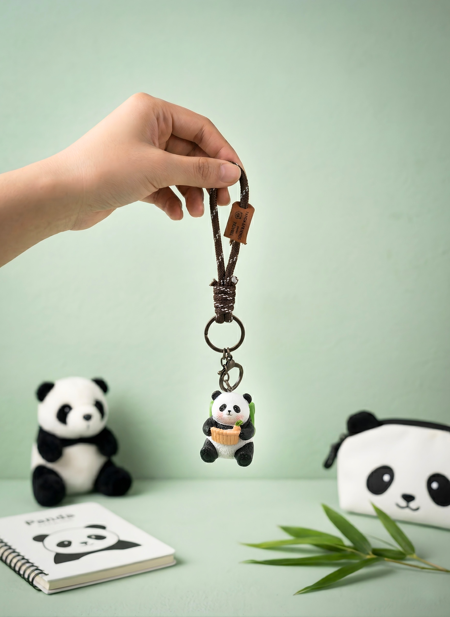 Hand holding a keychain with a panda design on a light green background