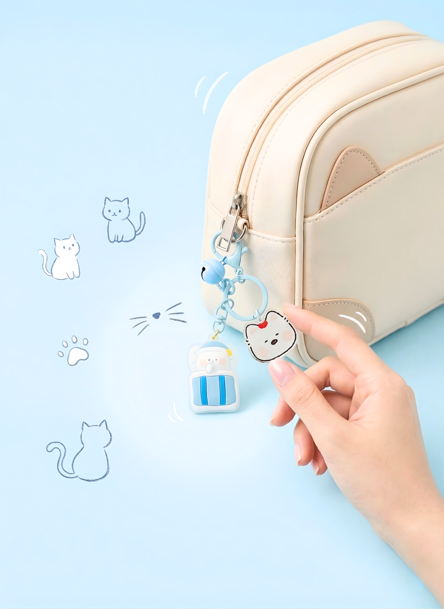 Hand holding a cute keychain with a cat design next to a beige pouch on a light blue background.