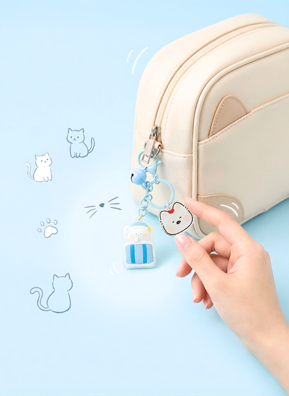 Hand holding a cute keychain with a cat design next to a beige pouch on a light blue background.