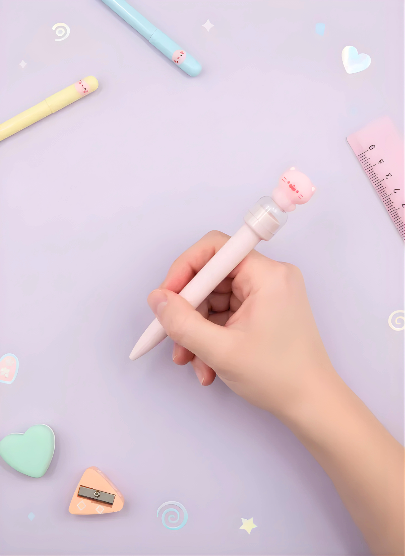 Hand holding a pink pen with a cartoon character on a light purple background with stationery items.