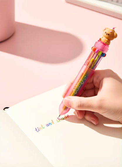 Hand holding a colorful pen with a bear-shaped top on a pink surface.