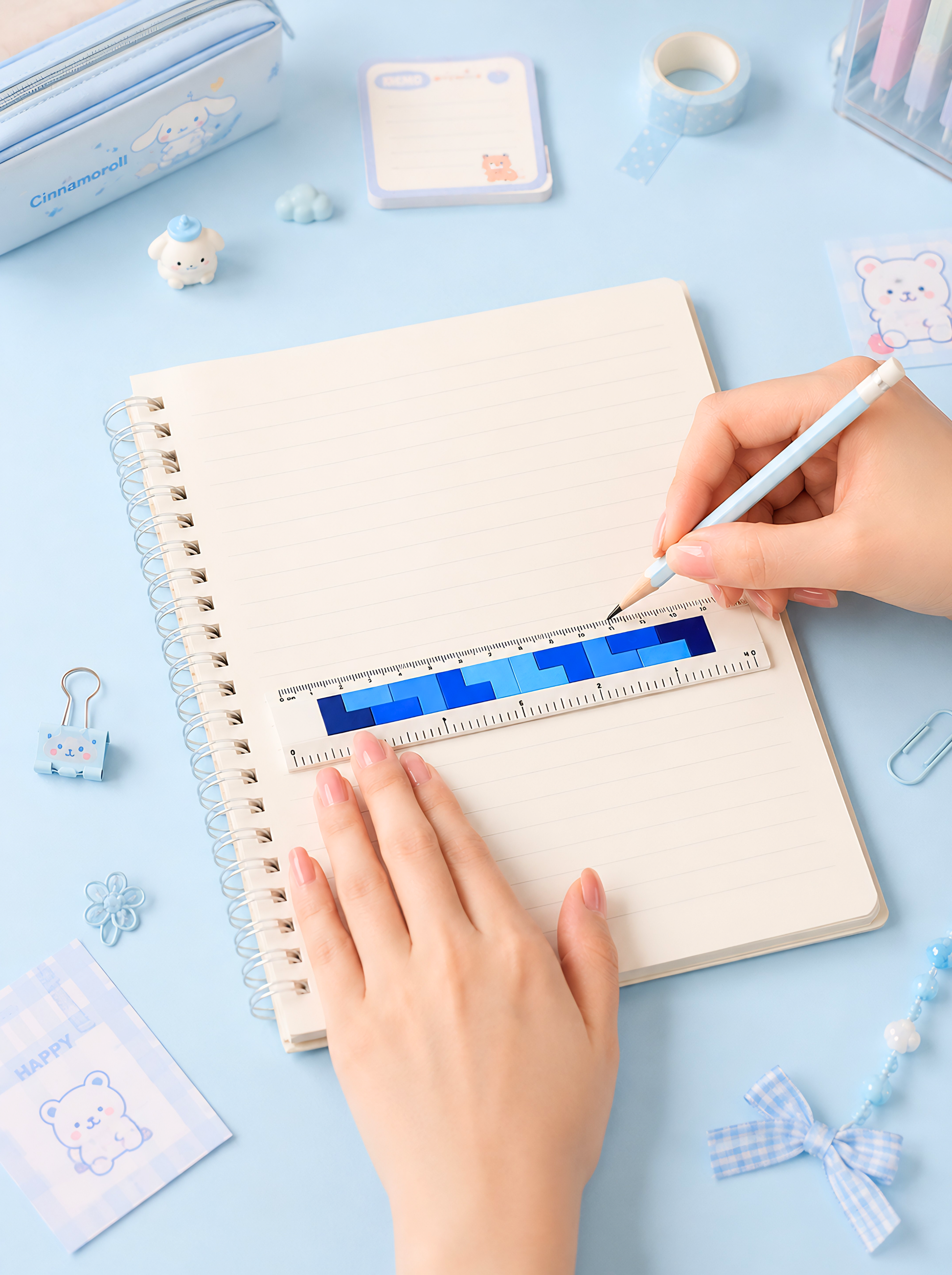 Person using a small ruler on a notebook with stationery items on a light blue background