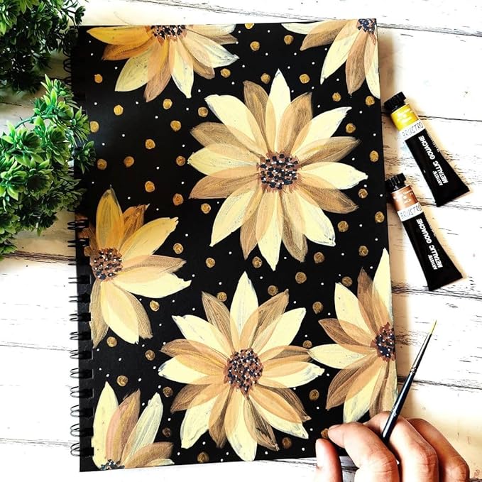 Notebook with floral design on a wooden surface with a hand holding a pen.