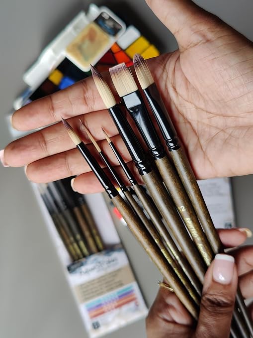 Hand holding a set of paintbrushes with a blurred art supply background