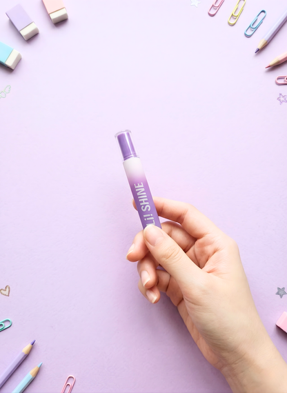 Hand holding a purple pen with 'SHINE' on a light purple background with stationery items.