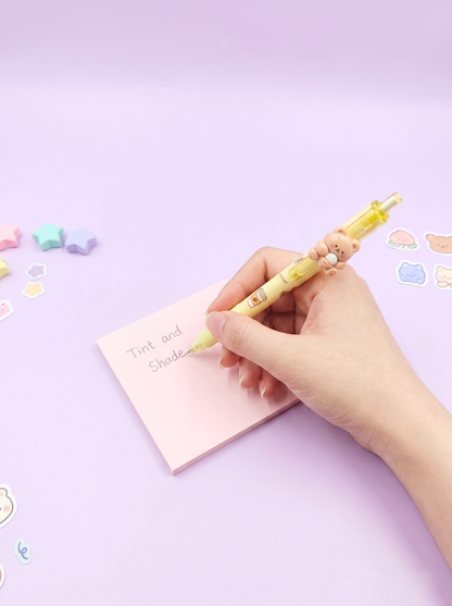 Hand holding a yellow pen over a pink notepad on a light purple background with colorful stickers.