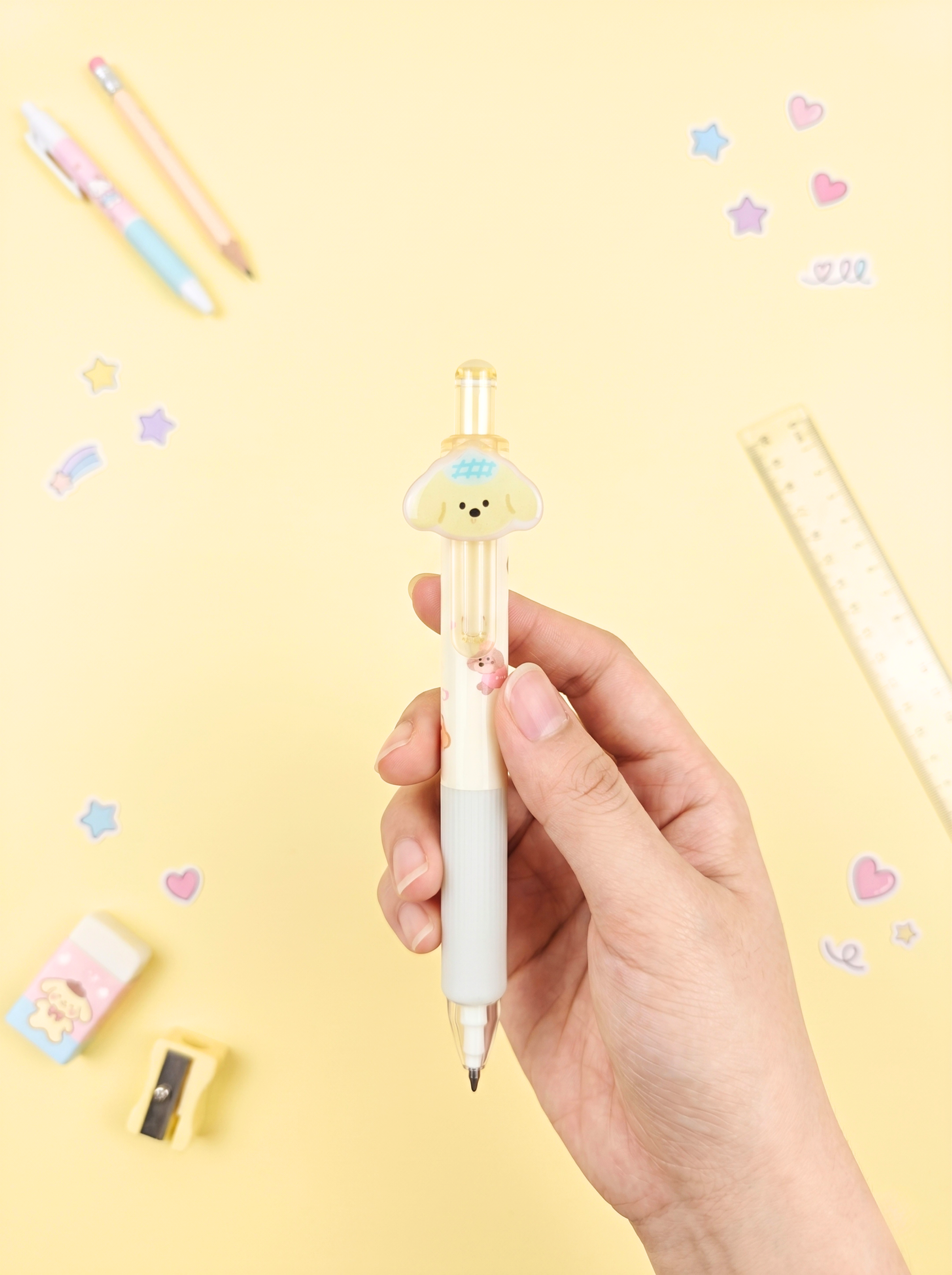 Hand holding a cute cartoon-themed pen on a yellow background with stationery items.