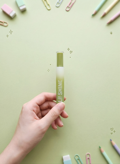 Hand holding a green and white pen with 'SHINE' branding on a light green background with stationery items.