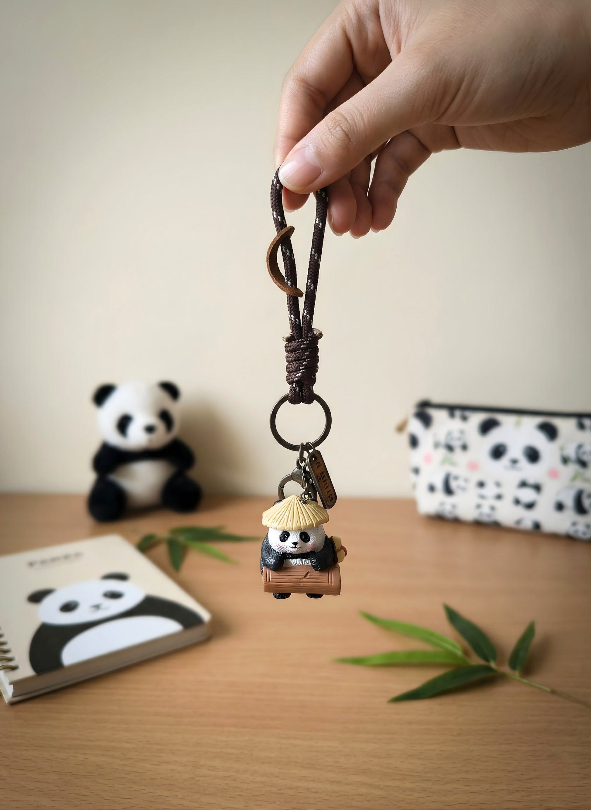 Hand holding a keychain with a panda design on a wooden surface.